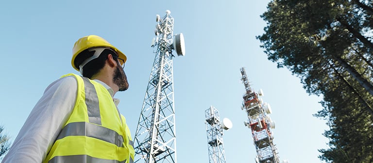 Homem engenheiro olhando para torres de telecomunicações emitindo radiofrequência para antenas.